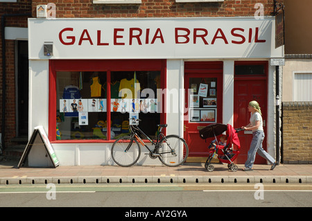 Une femme pousse un enfant dans une poussette devant le magasin Galeria Brasil sur Cowley Road à Oxford, Angleterre, Royaume-Uni. Banque D'Images