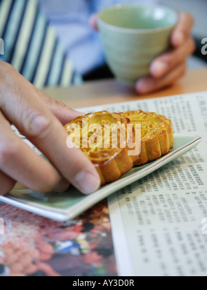Close-up of a person's une main agrippant un gâteau et l'autre main tenant une tasse de thé Banque D'Images
