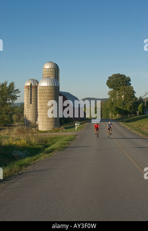 Deux hommes le vélo de route en montée sur une fin de l'été passé cet après-midi, une grange avec trois silos à Waitsfield Vermont Banque D'Images