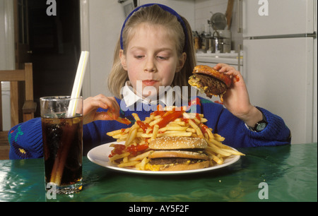 Jeune adolescente mangeant des fast-Foods malsains, un énorme hamburger et des chips buvant du coke à la maison dans après l'école Londres HOMER SYKES Banque D'Images