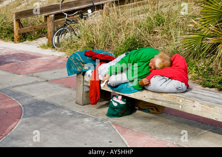 Femme de dormir sur un banc dans les vêtements de couleur à côté d'un trottoir par une rampe en bois à Jacksonville Beach, Florida, USA Banque D'Images