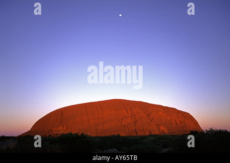 La lune sur Uluru Ayers Rock au lever du soleil dans le centre rouge dans les Territoires du Nord de l'Australie Banque D'Images