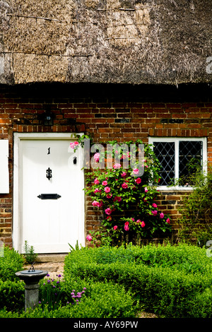 La porte avant, un toit de chaume et fenêtre d'un cottage anglais traditionnel avec de plus en plus roses roses sur la porte Banque D'Images