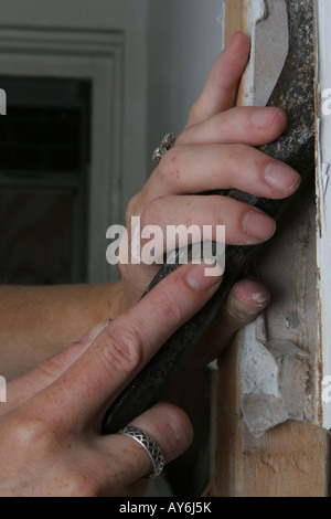 Woman's hands à l'aide de la gouge pour retirer le plâtre du mur Banque D'Images