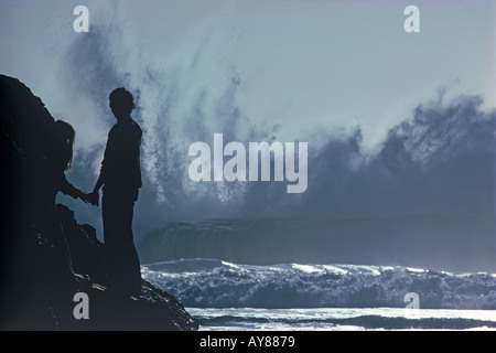 Les ondes de tempête battant Big Sur rocky shore avec couple watching Banque D'Images