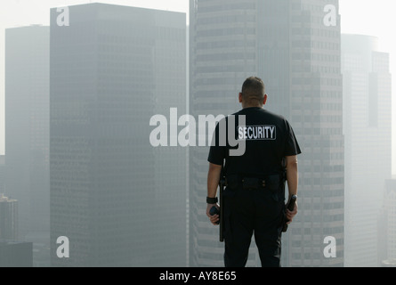 Agent de sécurité se tient sur le toit de l'immeuble de bureaux de grande hauteur donnant sur d'autres édifices du centre-ville de Los Angeles, CA Banque D'Images