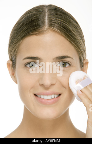 Femme en utilisant Powder Puff sur joue, smiling, portrait Banque D'Images