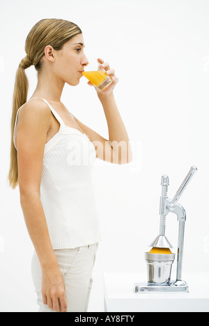 Jeune femme debout devant des presse-agrumes, de boire du jus d'orange fraîchement pressé Banque D'Images