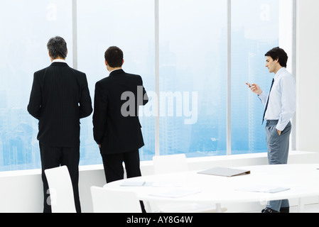 Businessmen standing par fenêtre dans la salle de conférence, un contrôle de cell phone Banque D'Images