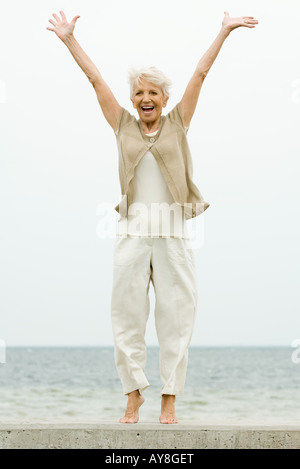 Hauts femme debout sur la pointe des pieds à la plage, bras levés, smiling Banque D'Images