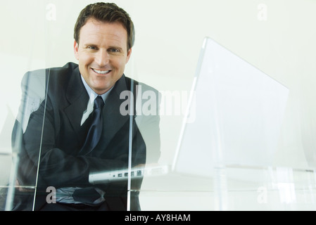 Businessman sitting next to laptop computer, smiling at camera Banque D'Images