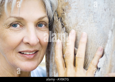 Senior woman leaning against tree trunk, smiling, portrait Banque D'Images