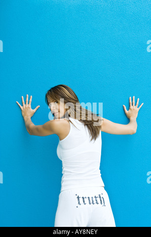 Femme en pantalon avec le mot "vérité" à l'arrière, debout avec les mains contre le mur, Banque D'Images