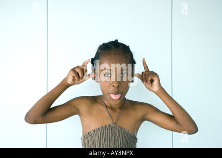 Little girl sticking tongue out at camera, bras levés, portrait Banque D'Images