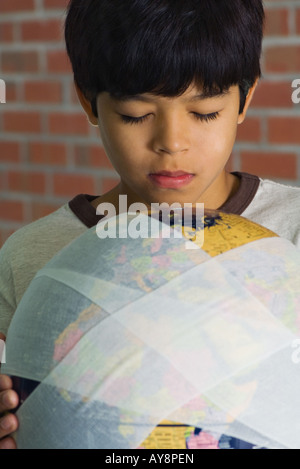 Boy holding globe enveloppé dans des bandages, les yeux clos, close-up Banque D'Images