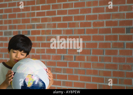 Boy holding globe enveloppé dans des bandages contre joue, les yeux fermés Banque D'Images