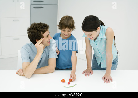 Son père et ses deux enfants dans la cuisine, faisant sourire hors de légumes Banque D'Images