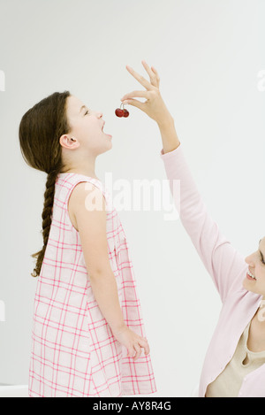 Femme accroupie avec un bras levé, l'alimentation fille cerises, side view Banque D'Images