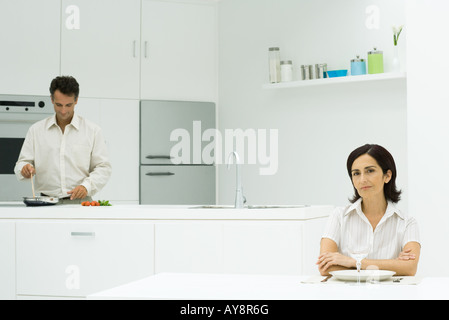 Femme assise à table avec les bras croisés, à la préparation de repas dans l'arrière-plan Banque D'Images