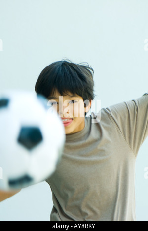 Petit Garçon jouant avec un ballon de football, les bras, smiling at camera Banque D'Images