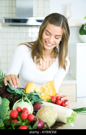 Jeune femme dans la cuisine, en regardant un assortiment de légumes frais, smiling Banque D'Images