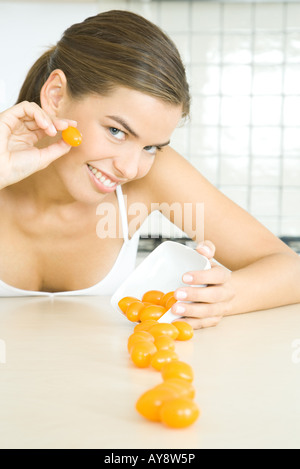Jeune femme déversant plat de tomates cerise, smiling at camera Banque D'Images