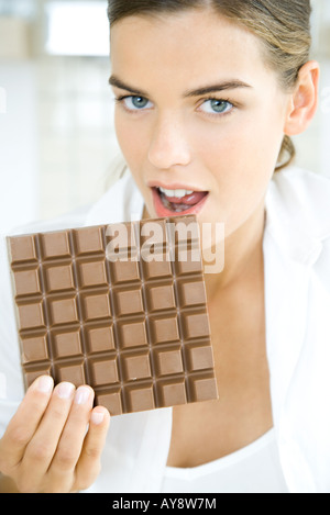 Woman biting en grande barre de chocolat, looking at camera Banque D'Images