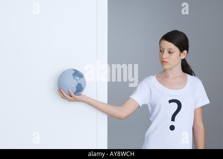 Girl wearing tee-shirt imprimé avec point d'interrogation, looking at globe Banque D'Images