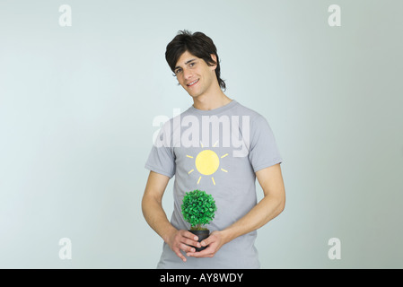 Jeune homme portant un tee-shirt avec graphique, holding potted plant, smiling at camera Banque D'Images