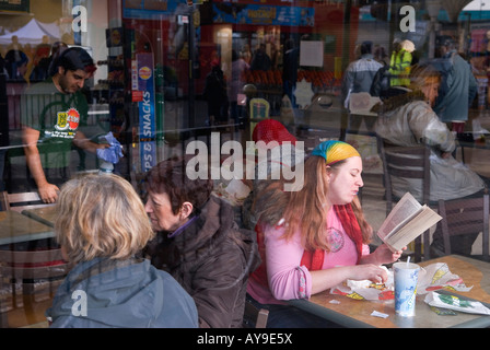 Femme en rose avec une écharpe couleur arc-en-ciel tenant ses cheveux en place. Livre de lecture dans le magasin de restauration rapide Londres années 2008 2000 Royaume-Uni HOMER SYKES Banque D'Images