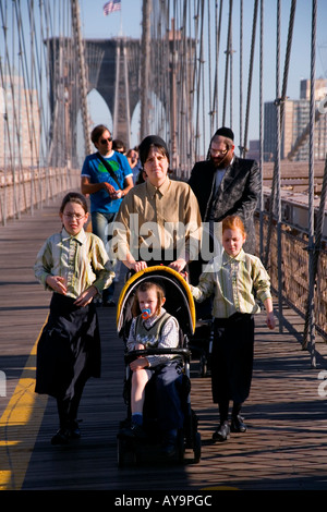 Une femme juive orthodoxe vêtu sévèrement pousse une poussette à travers le pont de Brooklyn à Manhattan New York remarque son mari Banque D'Images