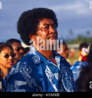 Portrait de teint foncé soleil fidjien mâle avec fuzzy typique des cheveux noirs en chemise bleu et blanc tropicales plusieurs personnes au-delà Banque D'Images
