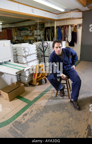 Portrait d'un homme assis sur un tabouret dans un entrepôt Banque D'Images