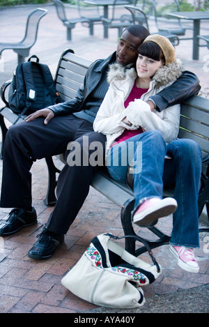 Inter-raciale contemplative young couple embracing on a park bench Banque D'Images