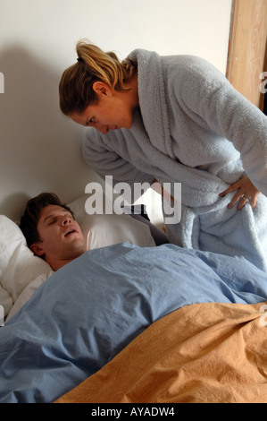 Angry young woman standing by bed en criant à son mari le ronflement sommeil Banque D'Images