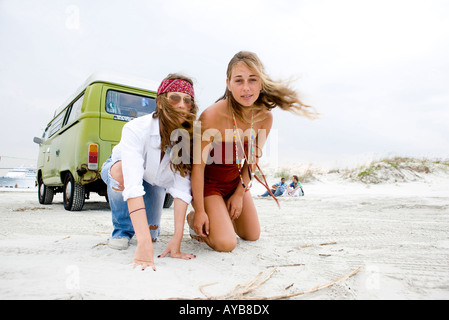 Portrait de jeunes femmes à la mode hippie à genoux sur le sable derrière van at beach Banque D'Images