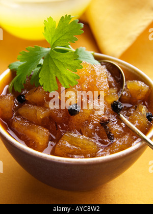 Un bol de chutney d'ananas avec une cuillère en laiton sur fond jaune Banque D'Images