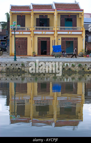 Homme avec brouette et 3 terrasse chambre jaune pastel reflète dans une ville historique de la rivière Hoi An milieu Vietnam Banque D'Images