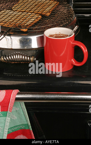 Grillage du pain sur la plaque chauffante d'un aga avec une tasse de boisson chaude rouge au chaud sur le dessus Banque D'Images