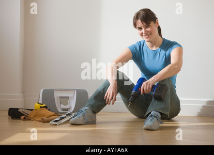 Woman sitting on floor holding perceuse sans fil Banque D'Images