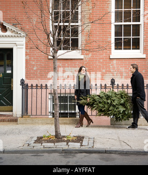 Couple carrying Christmas Tree on urban sidewalk
