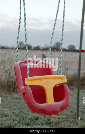 Childs red swing ralenti siège au début morming frost avec le paysage en arrière-plan Banque D'Images