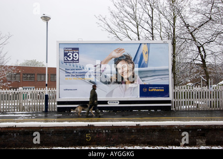 titan publicité panneau d'affichage sur la gare ferroviaire avec Lufthansa publicité de vacances de la compagnie aérienne avec la neige, et avec l'homme et le chien marchant devant Banque D'Images
