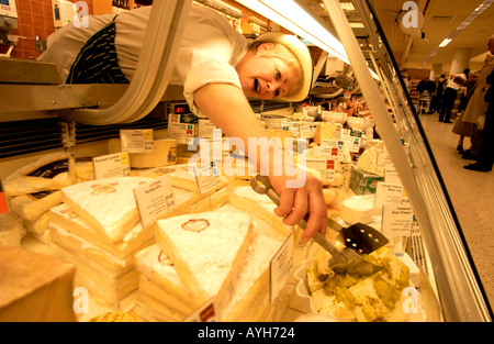 Un assistant de charcuterie en uniforme et hat s'étend pour atteindre le fromage sur son comptoir de charcuterie au supermarché Waitrose Banque D'Images