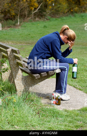 Femme avec un problème d'alcool assis sur banc de parc avec du vin et des bouteilles de bière Banque D'Images