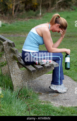 Femme avec un problème d'alcool assis sur banc de parc avec du vin et des bouteilles de bière Banque D'Images