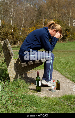Femme avec un problème d'alcool assis sur banc de parc avec du vin et des bouteilles de bière Banque D'Images