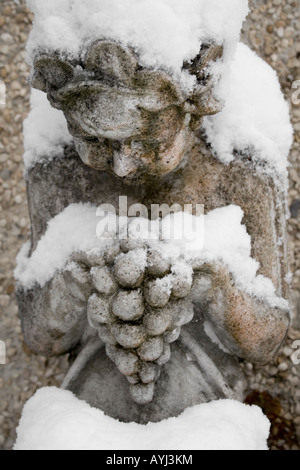 Statue de jardin offrant des raisins pendant une chute de neige de printemps dans l'Oxfordshire Banque D'Images