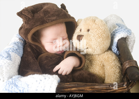 Un nouveau-né vêtu d'un ours en costume se défait dans un panier avec un ours en peluche. Banque D'Images