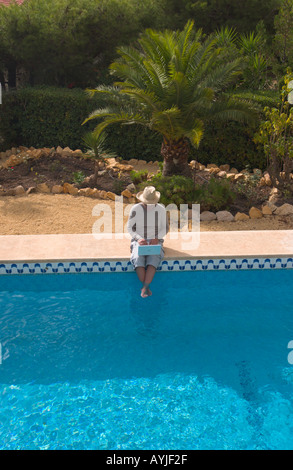 Homme assis au bord d'une piscine extérieure fonctionne sur ordinateur portable Banque D'Images